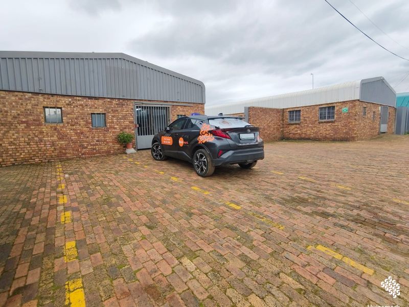 Commercial property exterior featuring a face brick facade, corrugated metal roofing, and a paved parking area with marked bays.