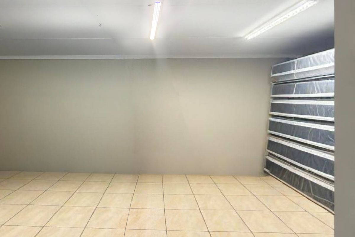 A clean, empty utility space featuring neutral tiled flooring and functional overhead fluorescent strip lighting, suitable for storage or workspace use.