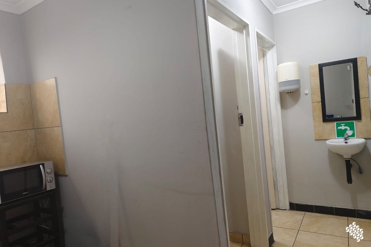 A functional commercial bathroom area featuring a wall-mounted basin, tiled splashback, and neutral finishes.