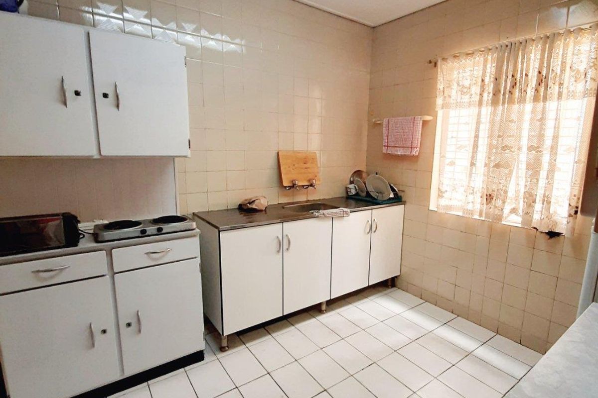 A functional kitchen featuring tiled walls and flooring, built-in white cabinetry, and a stainless steel sink, offering a dated but practical workspace.