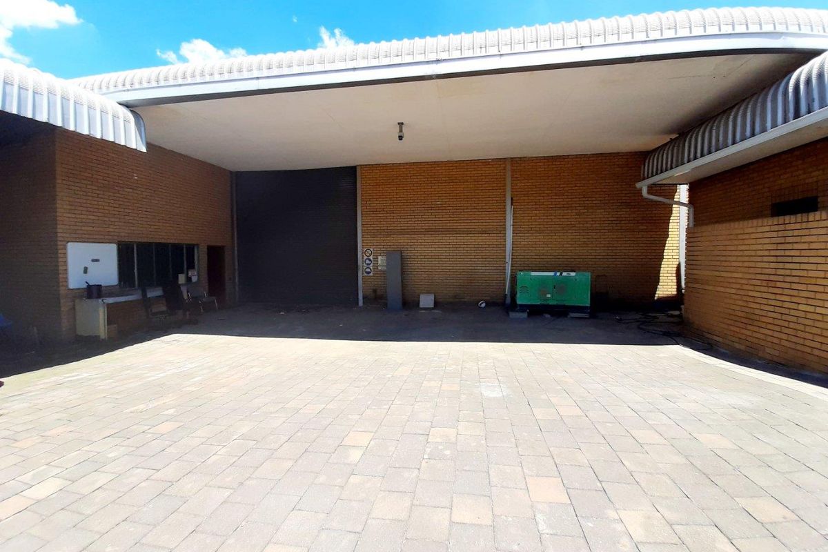 A paved commercial rear courtyard featuring a covered loading area with a roller shutter door and face brick exterior walls.