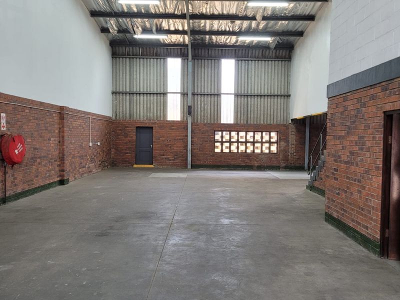 Spacious industrial warehouse unit featuring exposed steel roof trusses, durable concrete flooring, and brick wall finishes, suitable for various commercial or storage applications.