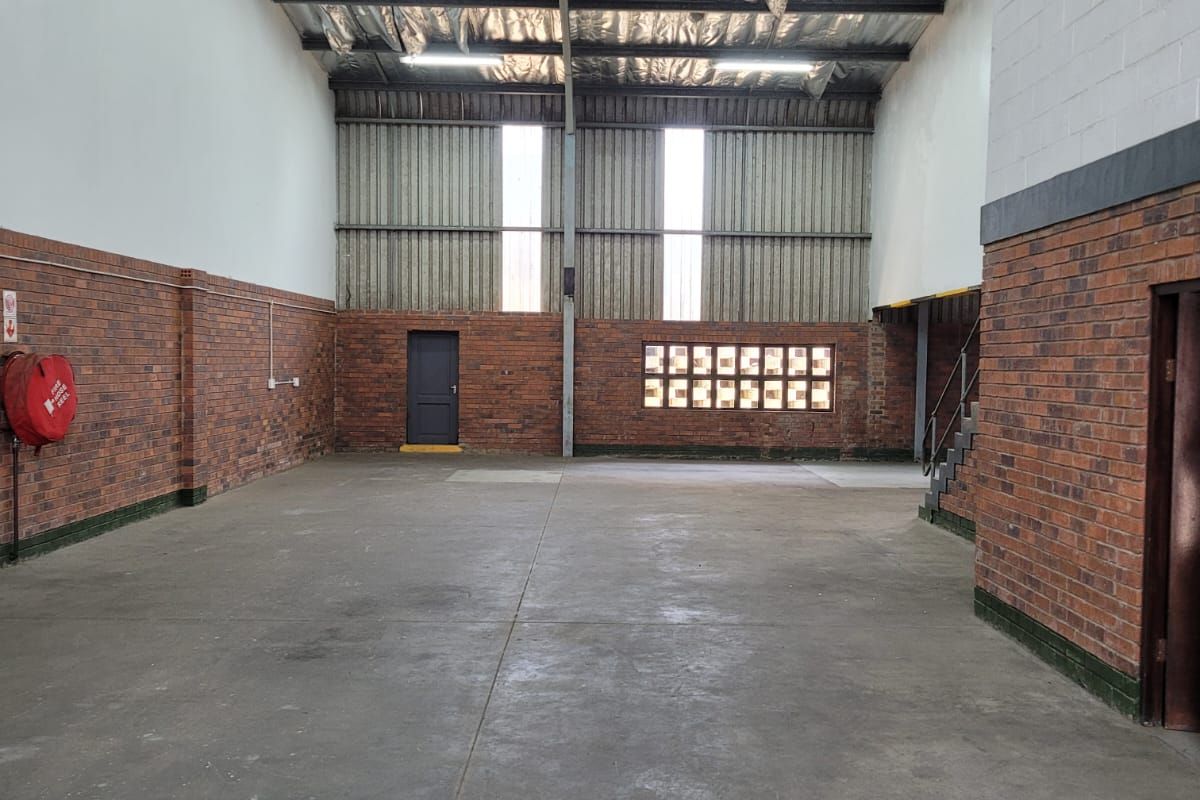 Spacious industrial warehouse unit featuring exposed steel roof trusses, durable concrete flooring, and brick wall finishes, suitable for various commercial or storage applications.