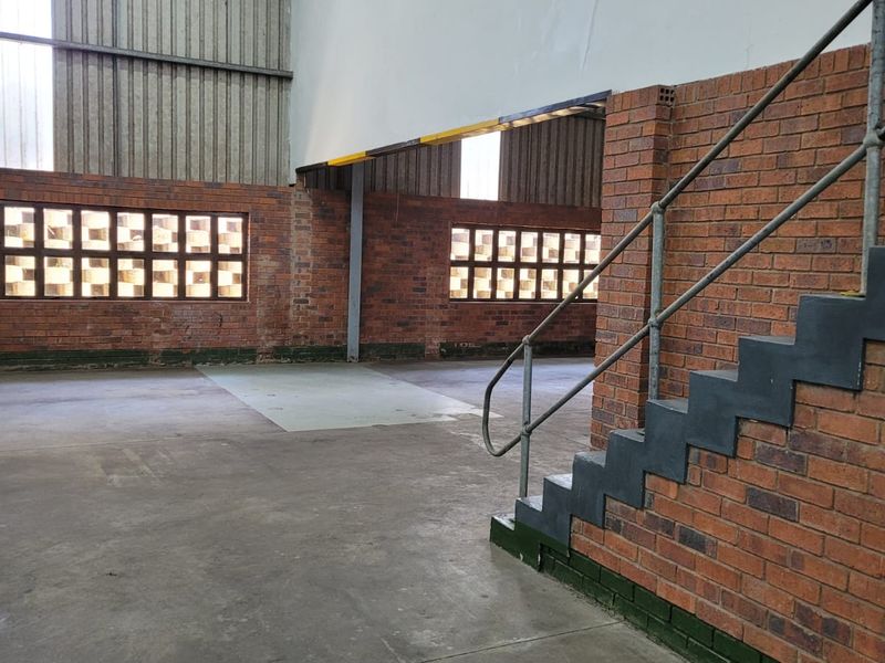 Spacious industrial utility area featuring exposed brick walls, concrete flooring, and a metal staircase leading to an upper level.