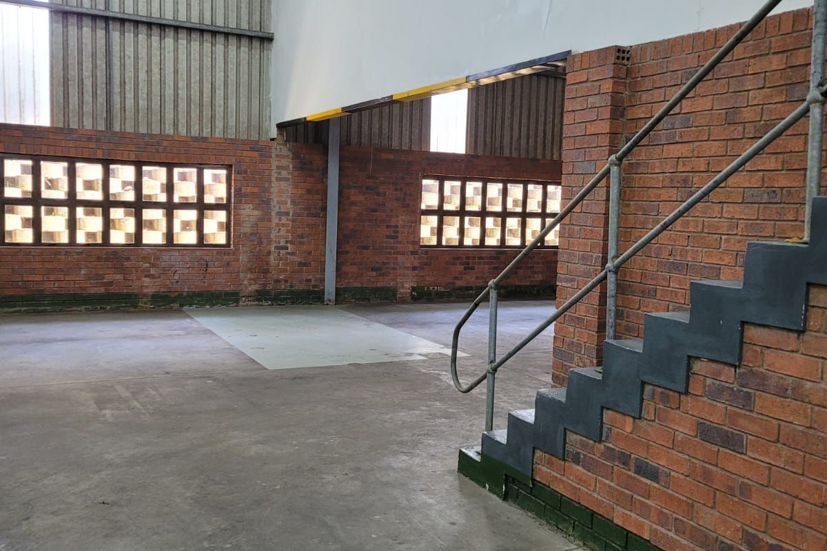 Spacious industrial utility area featuring exposed brick walls, concrete flooring, and a metal staircase leading to an upper level.
