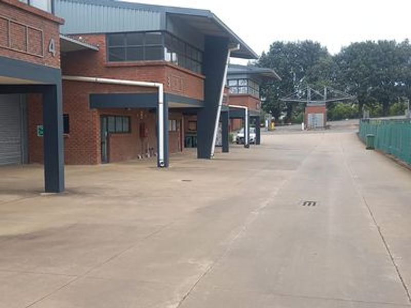 Industrial property exterior featuring multiple covered loading bays, brick facade construction, and a spacious concrete driveway for vehicle access.