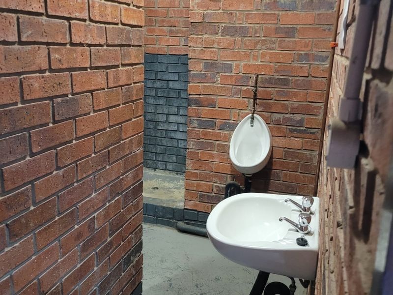 Industrial-style restroom featuring exposed brick walls, a wall-mounted basin, and a urinal, requiring cosmetic updates to improve the overall finish.