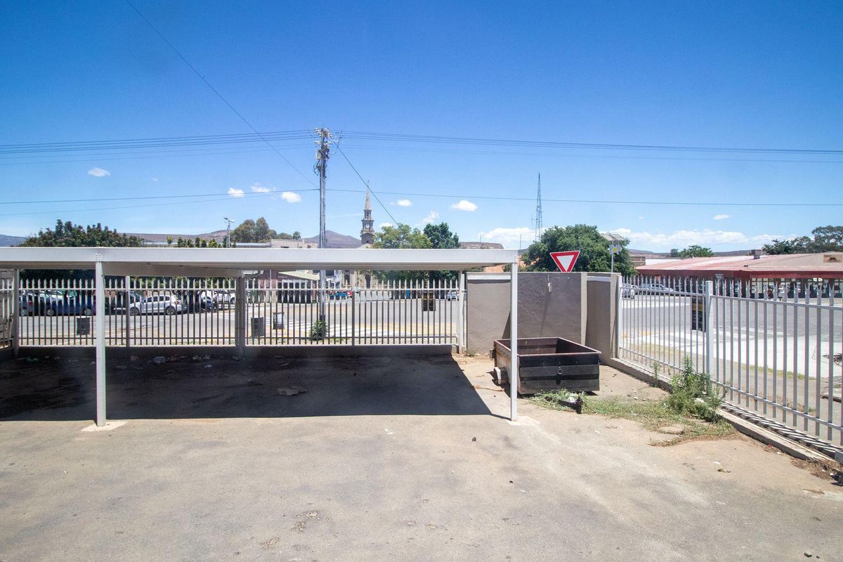 A paved commercial parking area featuring a covered carport structure and secure perimeter fencing.