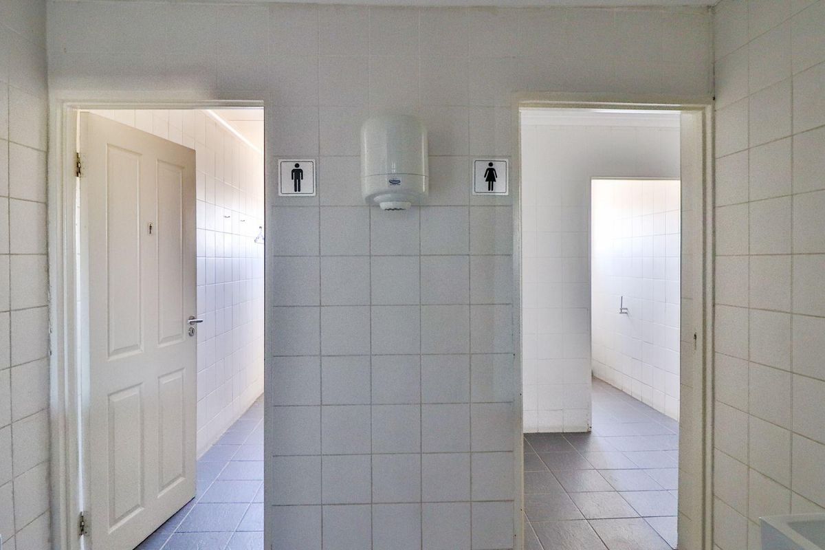 Commercial restroom facility featuring separate male and female entrances with tiled walls and flooring, equipped with wall-mounted hand dryer.