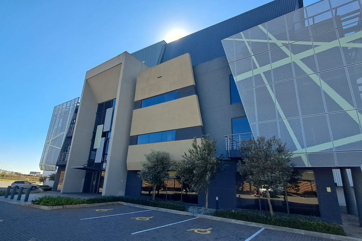 Modern industrial office building facade featuring decorative metal mesh panels, tinted glazing, and designated accessible parking bays.