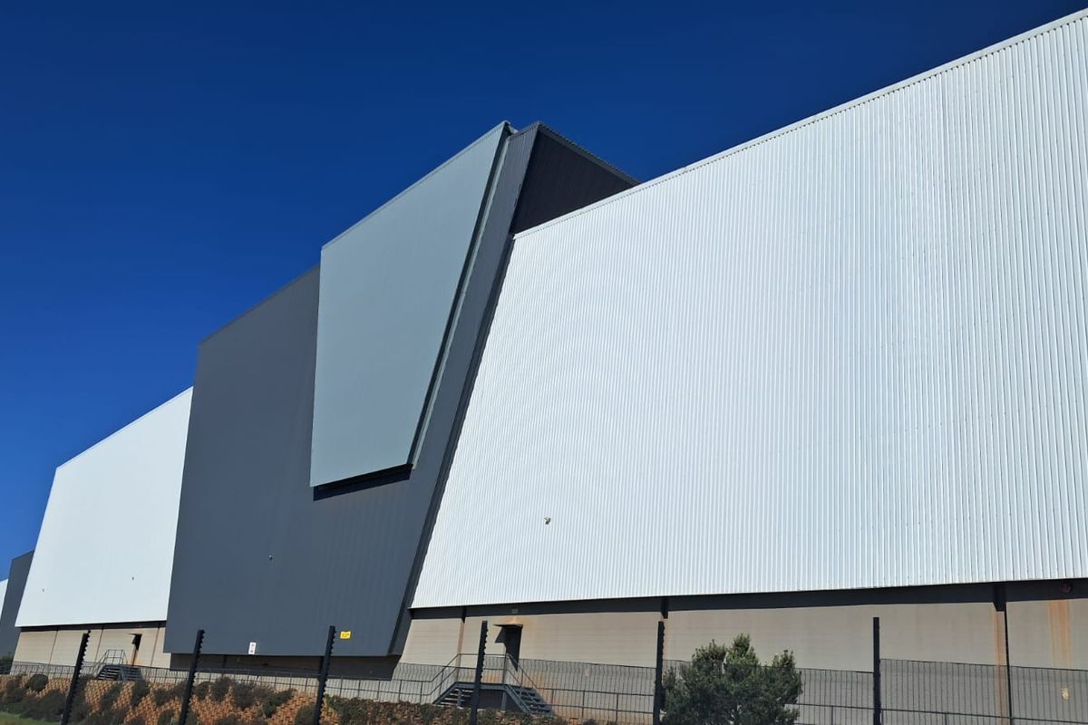 Modern industrial warehouse exterior featuring clean corrugated metal cladding, secure perimeter fencing, and a prominent architectural facade design.