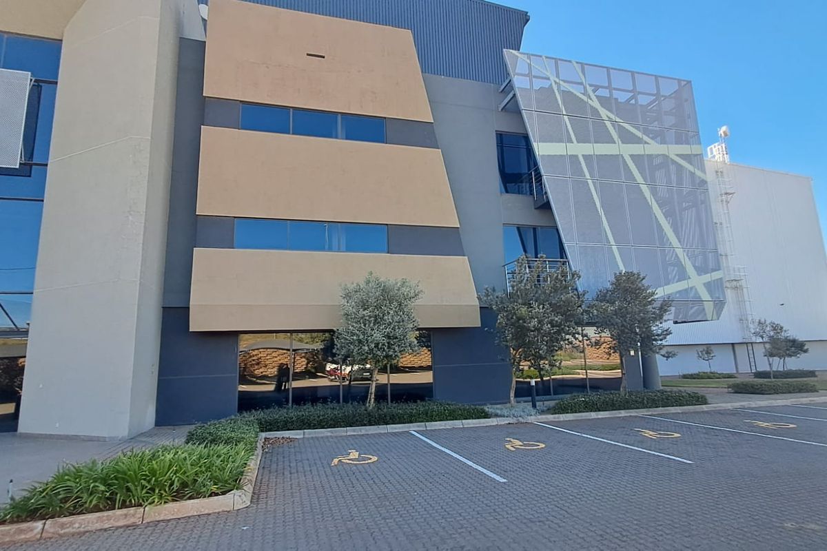 Modern industrial office building facade featuring extensive glass curtain walling, metal cladding, and dedicated paved parking bays.
