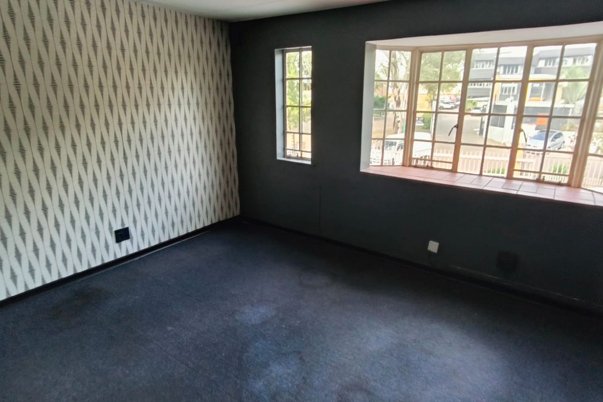 An empty room featuring dark carpeting, a patterned accent wall, and a large bay window providing natural light and street views.