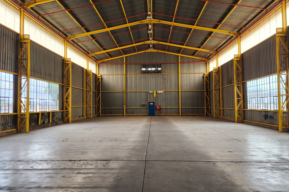Spacious industrial warehouse featuring high ceilings, exposed steel trusses, large steel-framed windows, and a durable concrete floor.