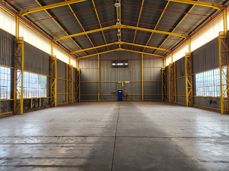 Spacious industrial warehouse featuring high ceilings, exposed steel trusses, large steel-framed windows, and a durable concrete floor.