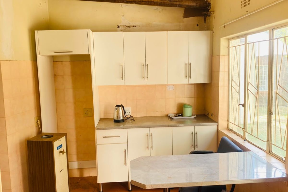 A functional kitchen area featuring white built-in cabinetry, laminate countertops, and tiled backsplash, with security bars installed on the window.