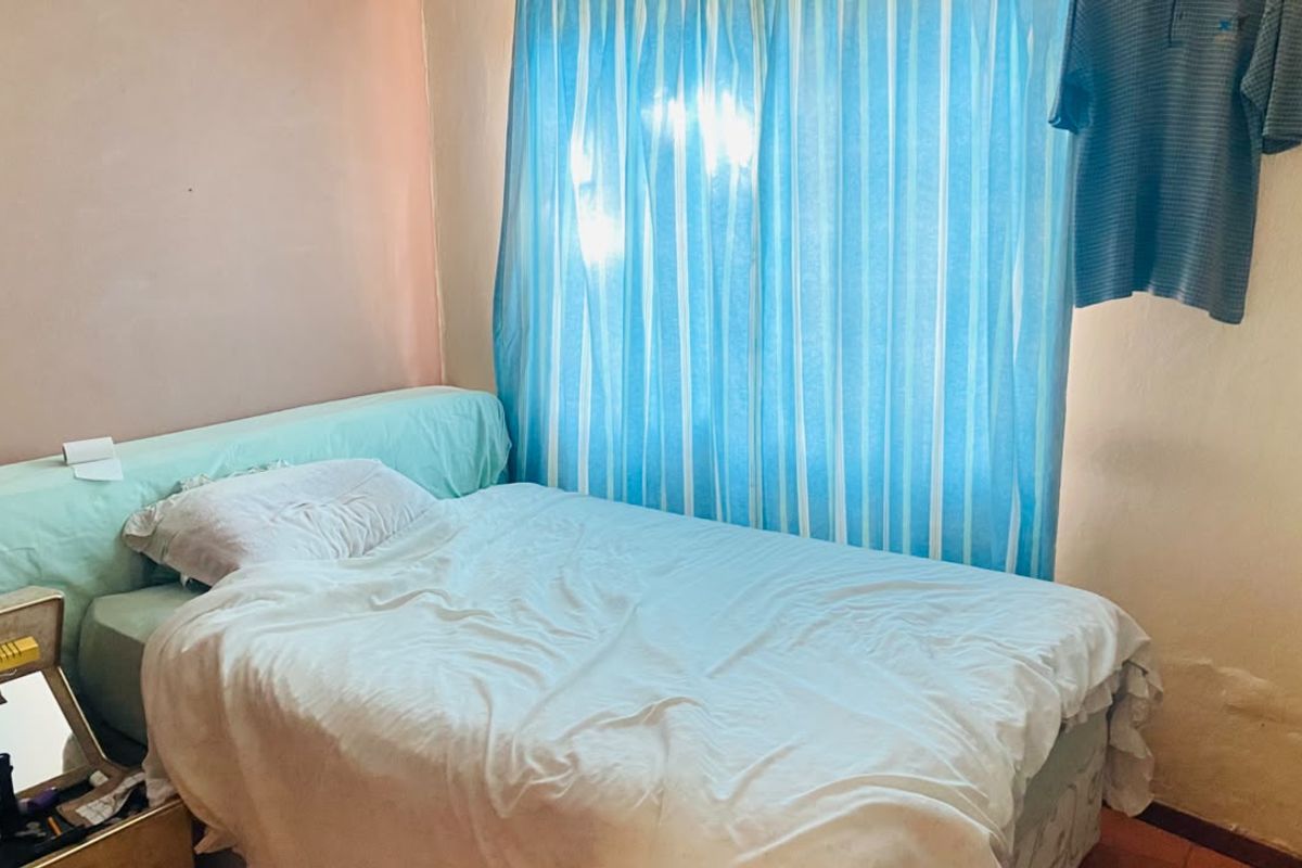 A bedroom featuring a window with blue curtains and visible wall surface wear, requiring cosmetic updates to improve the overall finish.