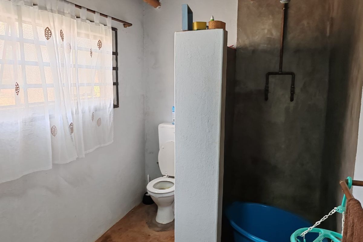 A rustic bathroom featuring a toilet and an open shower area with exposed copper piping and concrete wall finishes.