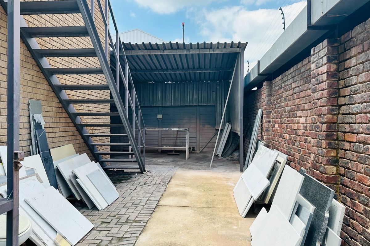 Rear exterior area featuring a metal staircase, corrugated roofing, and brick boundary walls with electric fencing.