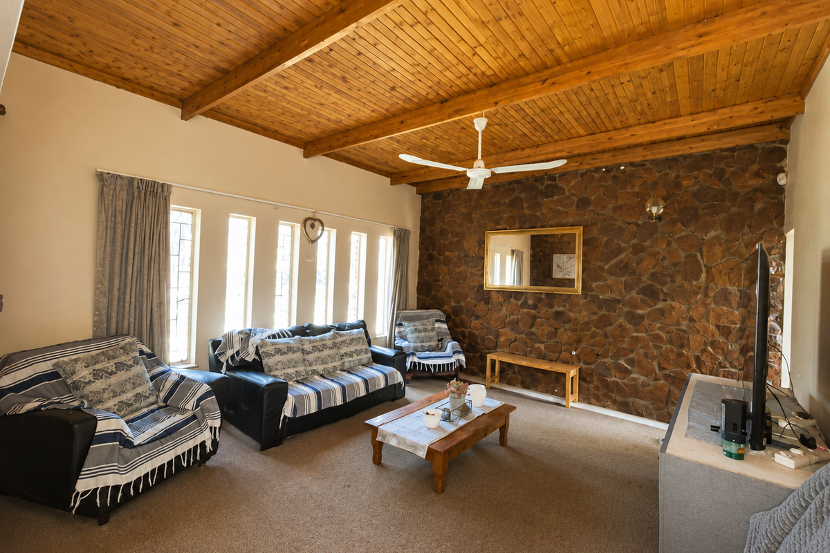 Spacious living room featuring a rustic stone accent wall, high exposed timber beam ceilings, and large windows providing ample natural light.