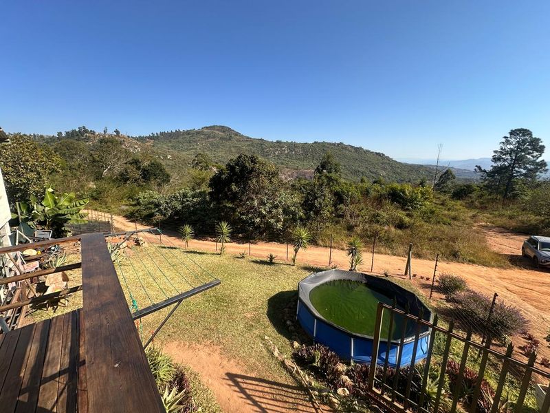 Elevated view from a wooden deck overlooking a rural landscape, garden area, and mountain scenery.