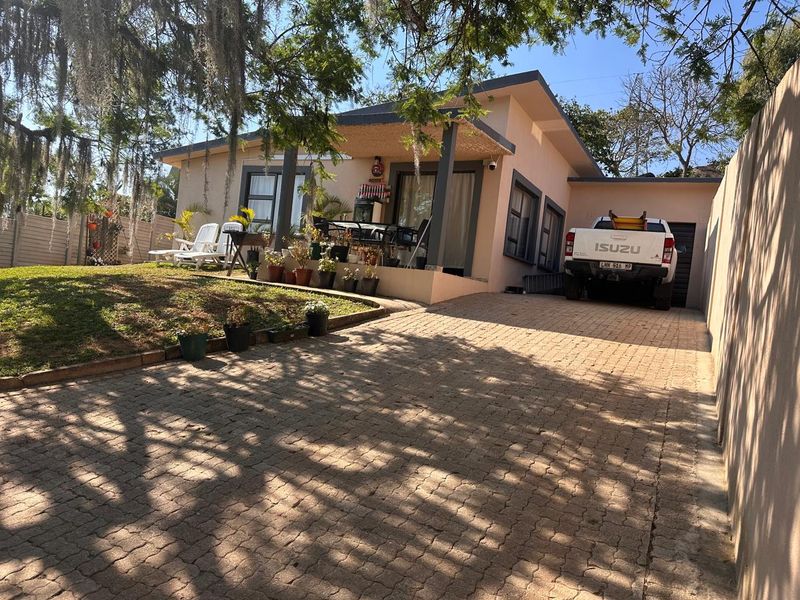 Front view of the property featuring a paved driveway, covered patio area, and attached garage, set within a landscaped garden.