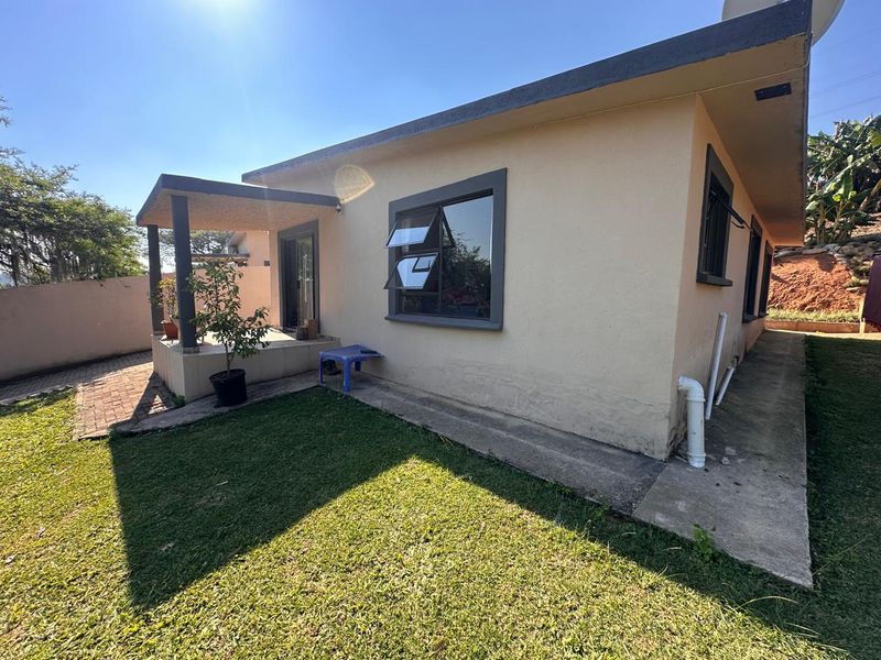 Rear view of the property featuring a covered patio, paved walkway, and established garden area with visible exterior wall finishes.