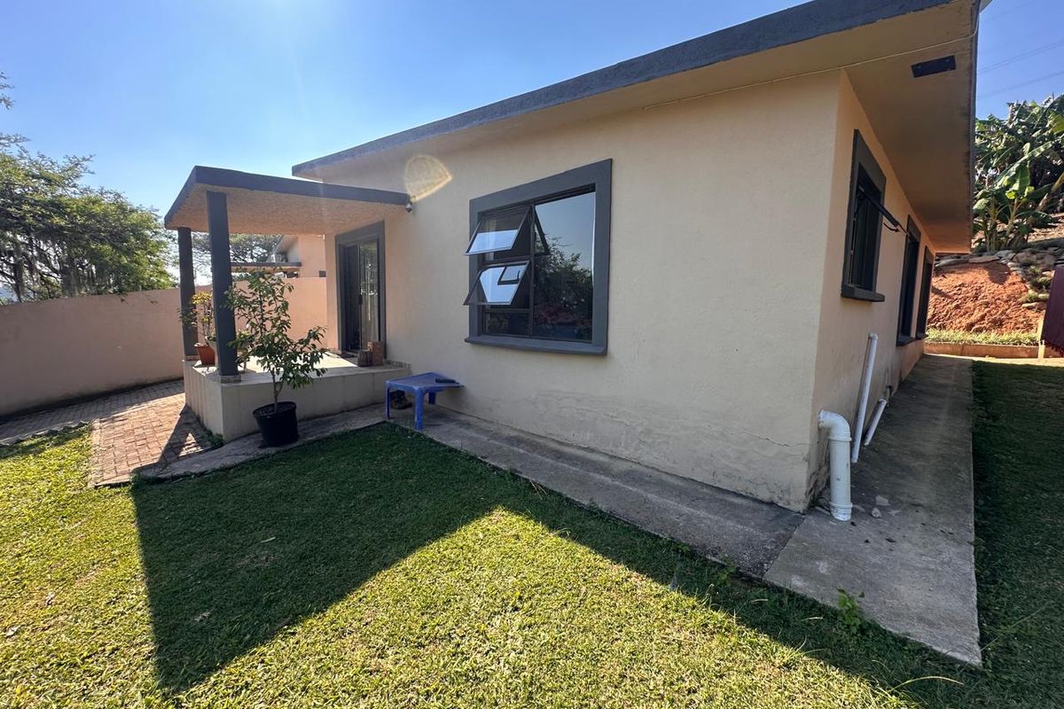 Rear view of the property featuring a covered patio, paved walkway, and established garden area with visible exterior wall finishes.