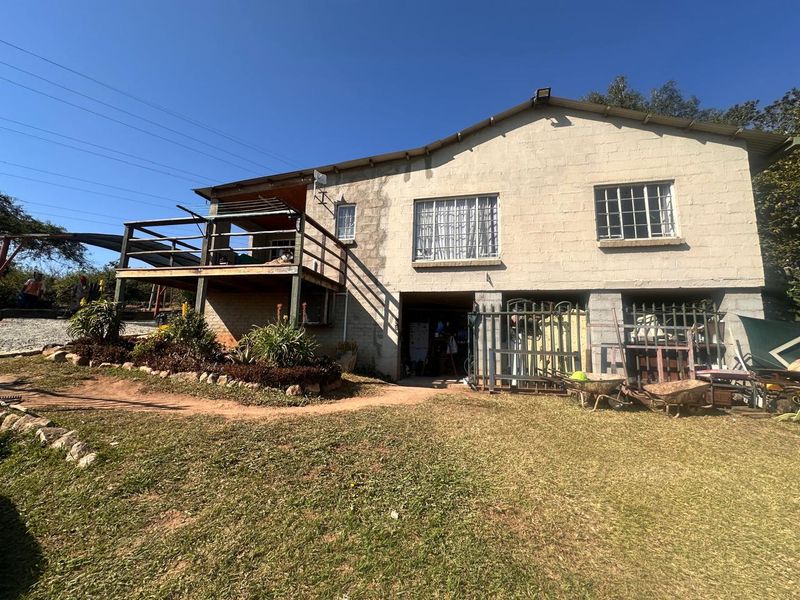 Rear view of a small holding property featuring a raised wooden deck, concrete block construction, and a large garden area with established landscaping.