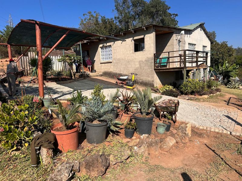 Rear view of a small holding dwelling featuring unfinished concrete block walls, a raised wooden deck, and a covered outdoor area with paved access.
