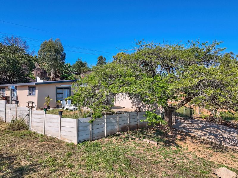 Rear view of the property featuring a precast concrete boundary wall, paved driveway, and established garden area with mature trees.