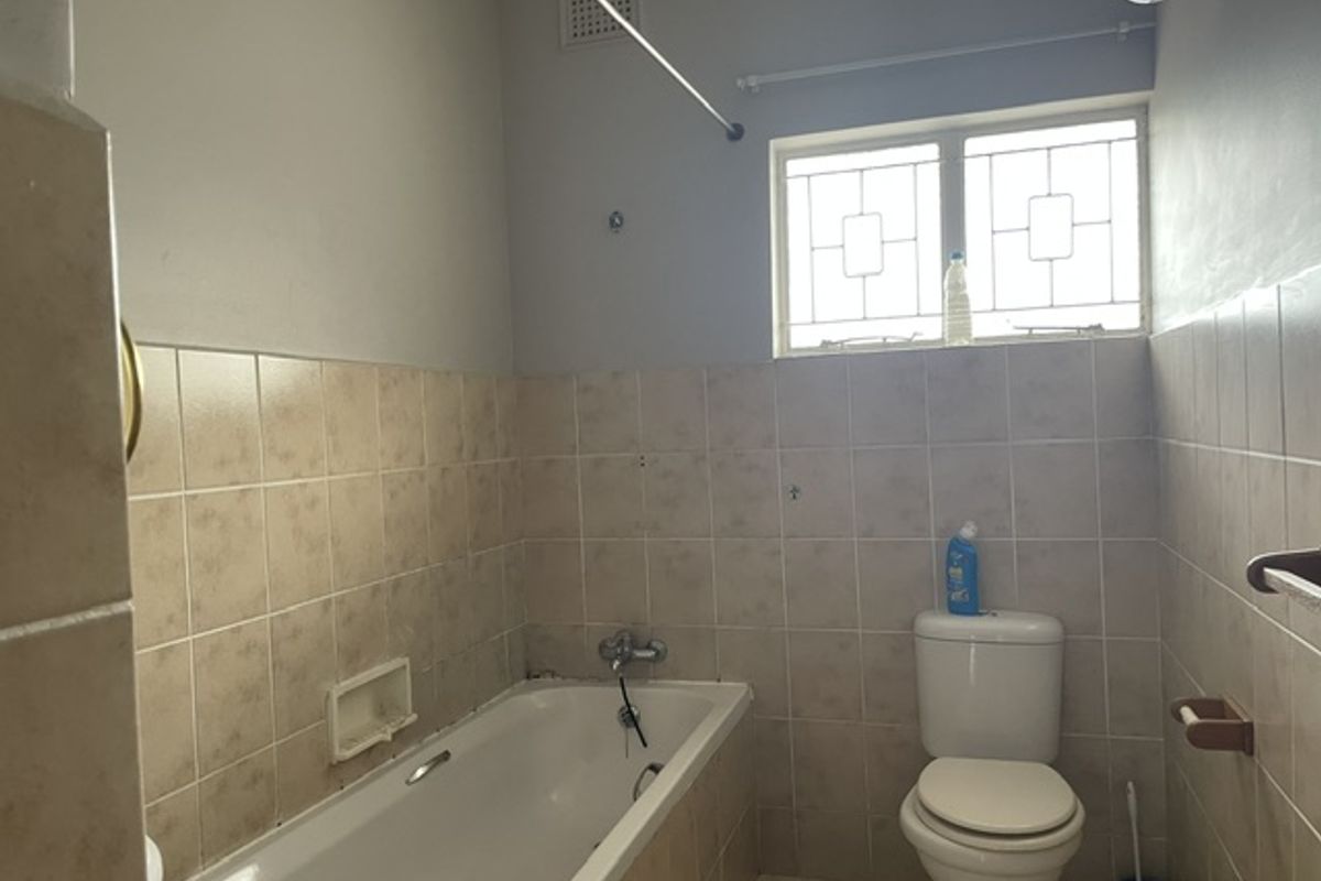 A functional bathroom featuring a standard bathtub, toilet, and tiled walls with a window providing natural light.
