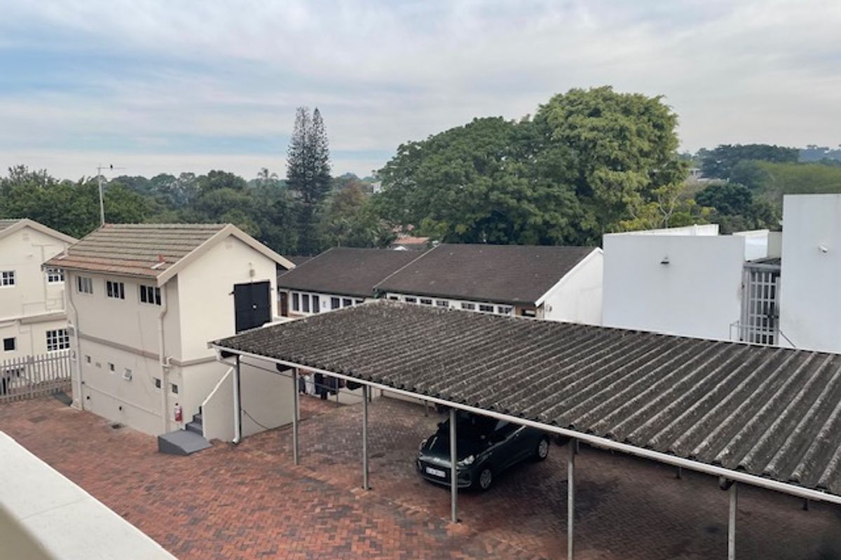 Elevated view of the office property grounds, featuring a paved courtyard, covered carport parking, and surrounding building structures.
