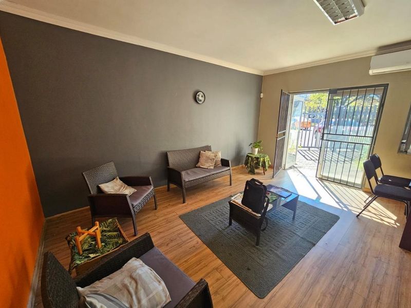 A commercial waiting area or reception space featuring laminate flooring, a split-system air conditioner, and direct access to the exterior via a security gate.