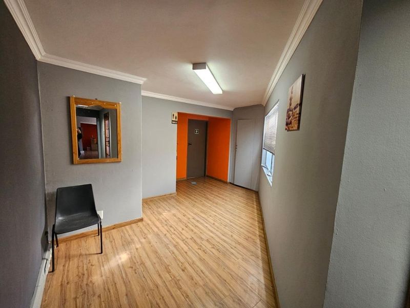 A clean, well-lit commercial hallway featuring durable laminate flooring, neutral grey walls, and a bright orange accent wall leading to a restroom.