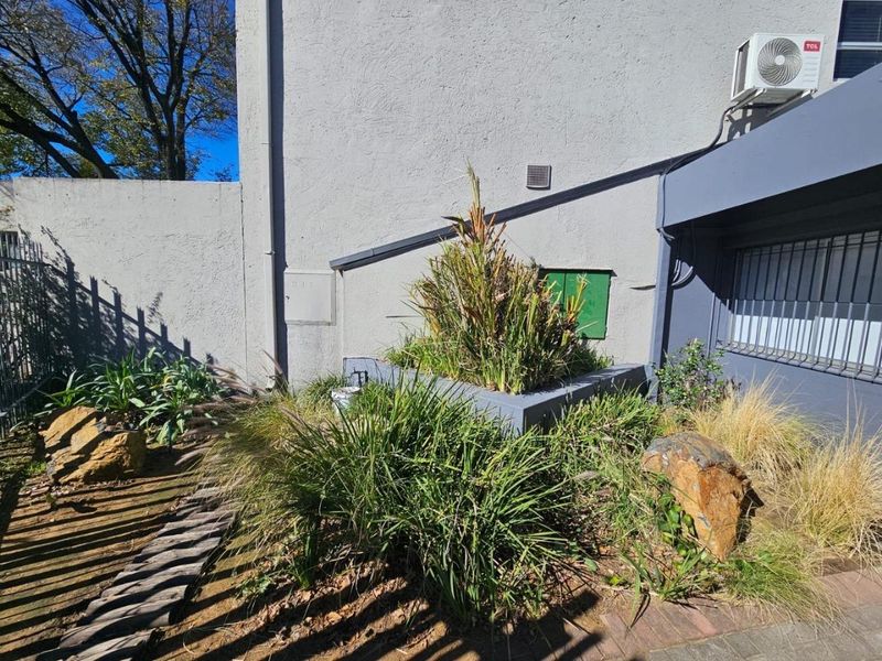 Rear exterior area featuring a raised garden bed, security bars on windows, and an external air conditioning unit against a rendered boundary wall.