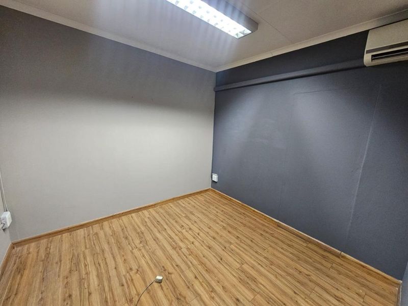 A clean, empty office space featuring wood-look laminate flooring, a wall-mounted air conditioning unit, and modern grey accent walls.