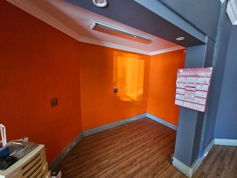 A vacant office space featuring laminate flooring, recessed lighting, and bright orange accent walls, suitable for a professional workspace.