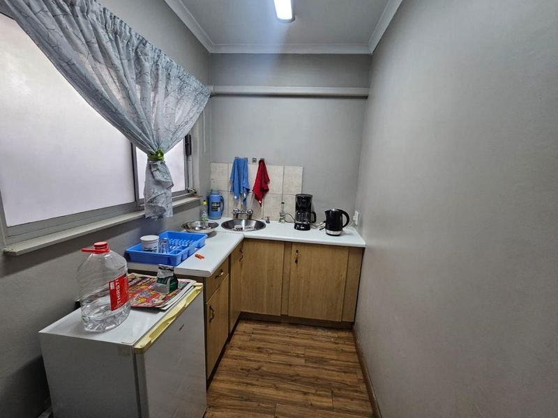 A compact scullery or kitchenette area featuring wood-look laminate flooring, built-in cabinetry, and a stainless steel sink with a tiled splashback.