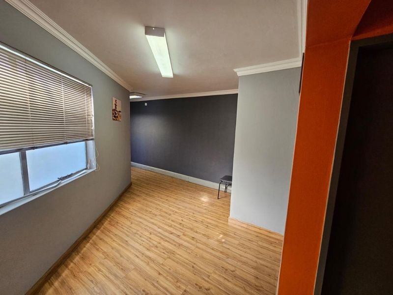 A clean, empty office space featuring laminate flooring, neutral wall tones, and functional window blinds, suitable for a professional workspace.