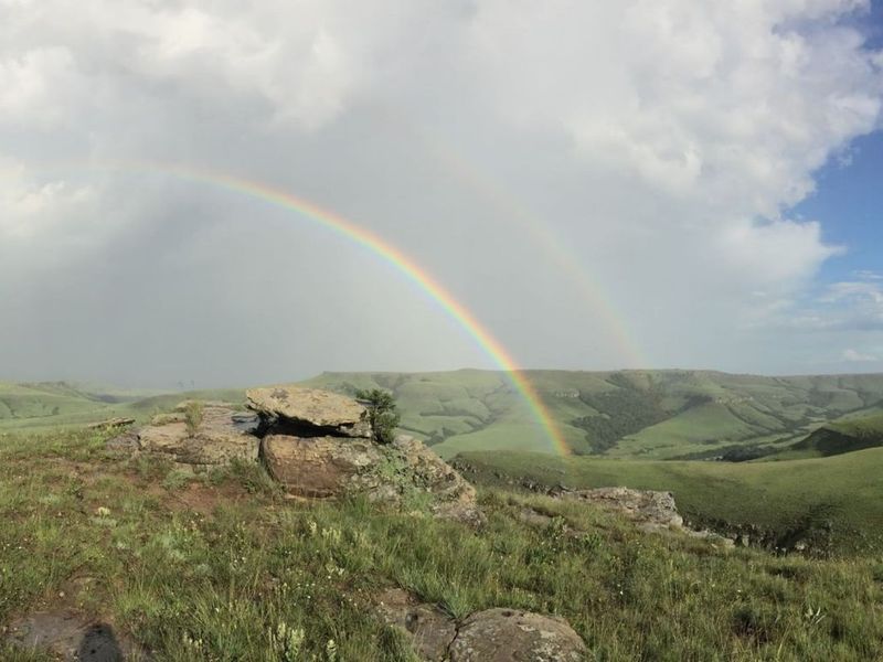 A scenic panoramic view of the rolling green hills and natural rock formations on the farm property under a rainbow.