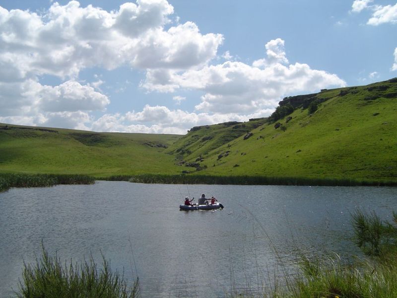 A scenic view of a natural farm dam surrounded by rolling green hills and grassy banks.