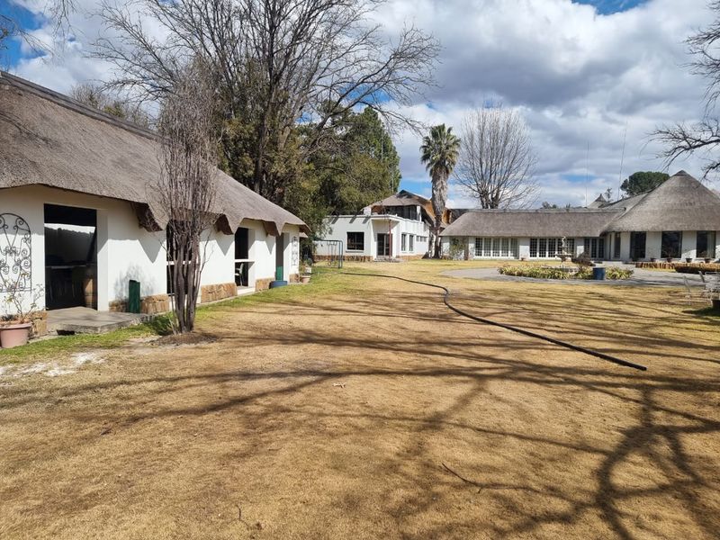 Spacious rear garden area featuring multiple buildings with traditional thatched roofs, a central paved courtyard, and established landscaping.