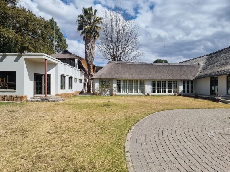 Rear view of a commercial property featuring a large lawn, paved driveway, and traditional thatched roof architecture with multi-pane windows.