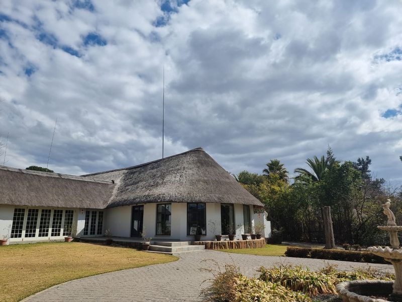 Rear view of a commercial property featuring a traditional thatched roof, paved driveway, and landscaped garden with a stone fountain.
