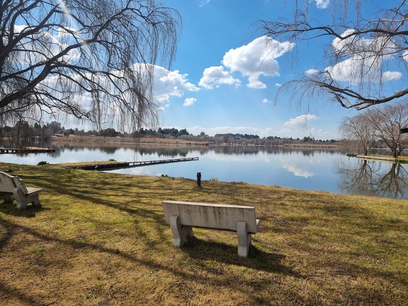 A scenic view of a tranquil lake featuring a wooden jetty, surrounded by landscaped grounds and mature trees.