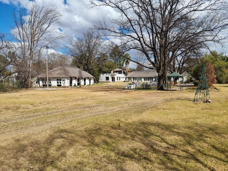 A wide view of the rear garden featuring multiple buildings with thatched roofs and a paved outdoor entertainment area.