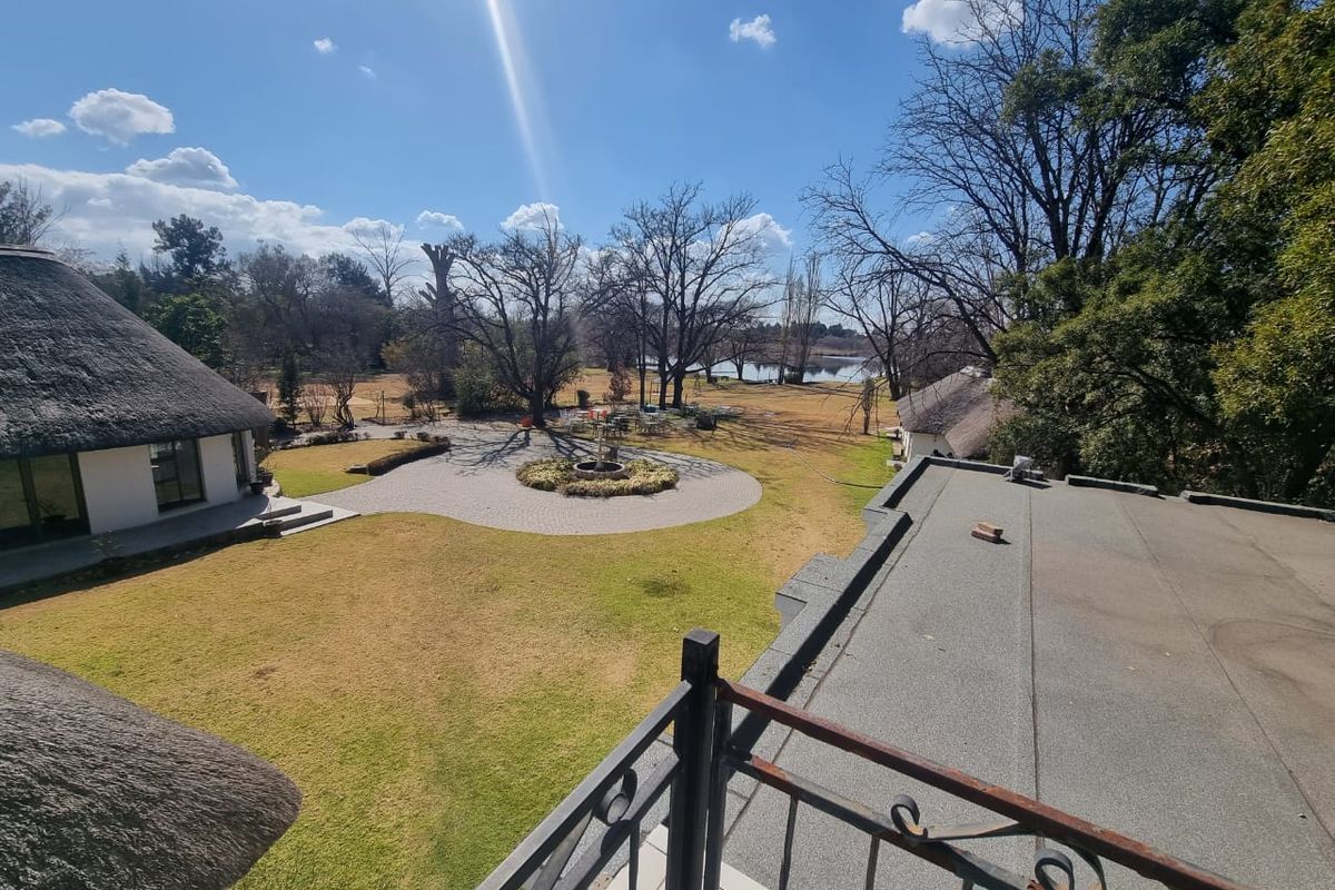 Elevated view of a commercial property grounds featuring thatched roof buildings, a paved circular driveway, and expansive garden space overlooking a water feature.