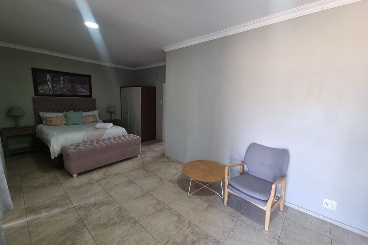 A spacious bedroom featuring neutral wall tones, tiled flooring, and recessed ceiling lighting, providing a clean and functional living space.
