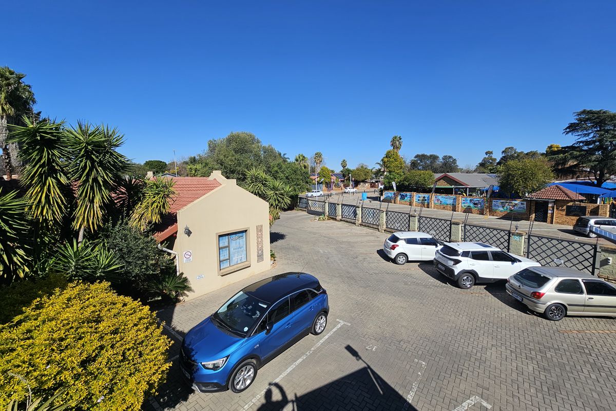 Elevated view of the office property exterior, featuring a paved parking area, perimeter fencing, and landscaped garden surroundings.